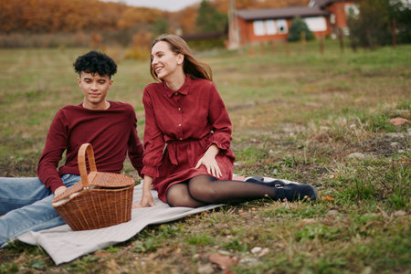 A candid outdoor moment captures two people sharing a simple picnic on a grassy field, genuine smiles, natural light, relaxed posture, and an authentic, wholesome vibe.の写真素材