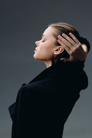 Calm woman with closed eyes in black coat expressing peacefulness and introspection on dark gray backgroundの写真素材