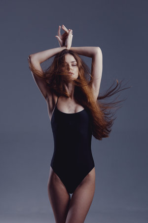 graceful woman in black swimsuit posing with closed eyes and flowing hair, serene expression, studio backgroundの写真素材