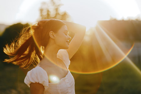 Young woman enjoying sunset outdoors, with flowing hair illuminated by golden sunlight, conveying...