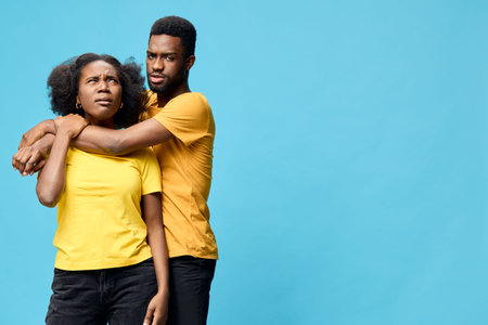 Couple in matching yellow shirts expressing confusion and concern against a bright blue background, showcasing emotional connection and casual styleの写真素材