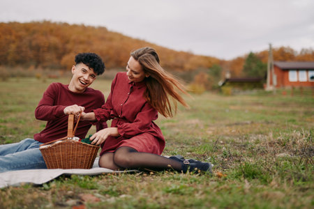 A genuine outdoor picnic scene showing an authentic couple sharing a wicker basket on a grassy field, relaxed interaction capturing natural smiles and true connection.の写真素材