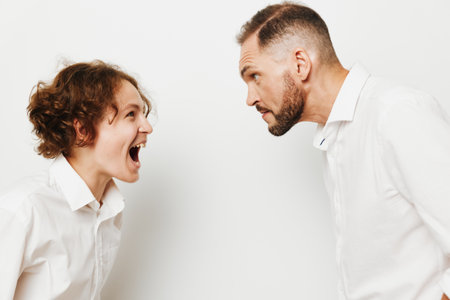 A professional business scene shows two people in white shirts arguing with intensity, standing against an isolated white background, expressing bold emotion and a tense confrontation.の写真素材