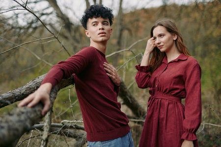 Young couple in matching burgundy outfits pose naturally outdoors, conveying genuine connection and relaxed presence, focused on real emotions and honest interaction in a rustic woodland setting.の写真素材