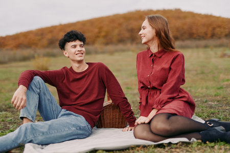 Candid outdoor portrait of a young couple sharing a genuine, authentic moment on a picnic blanket in an autumn field, conveying natural connection and quiet trust.の写真素材