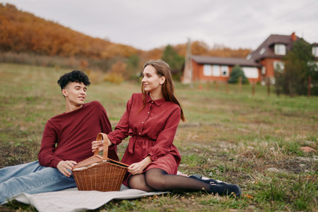A candid outdoor picnic scene with a couple on a blanket, a wicker basket nearby, autumn field and soft light creating an authentic, natural mood.の写真素材
