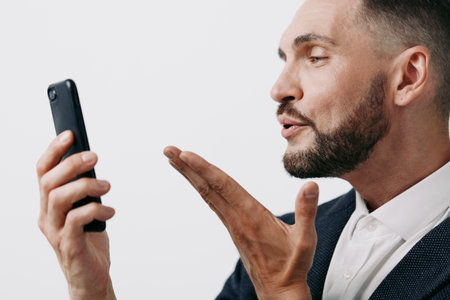A professional man in a suit speaks into a smartphone, showing focus and confidence against a clean colored background, an isolated setting that highlights his business persona and emotion.の写真素材