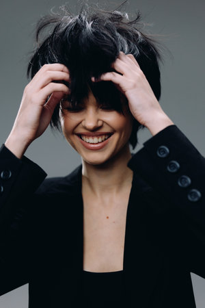 Smiling woman with messy hair wearing black blazer expressing joy and happiness in studio setting.の写真素材