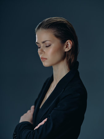 Thoughtful woman with eyes closed in black jacket expressing calm and introspection on blue backgroundの写真素材