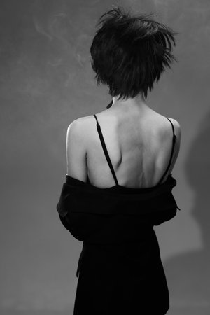 Black and white artistic portrait of a slender woman with short hair and exposed back in a dark outfit.の写真素材