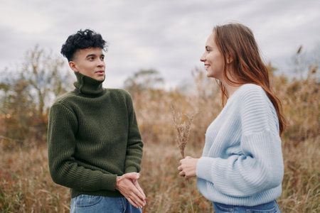 Two young adults share a sincere conversation in an autumn meadow, making steady eye contact and showing relaxed body language. Natural facial expressions convey genuine connection and dependableの写真素材