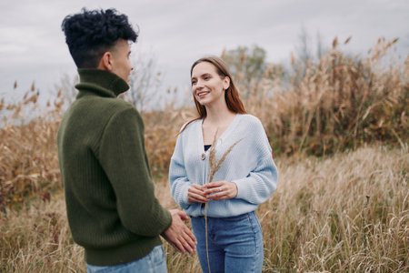 Genuine candid portrait of a young couple sharing a sincere moment in a windswept meadow, natural expressions and open interaction conveying a relatable outdoor connection.の写真素材