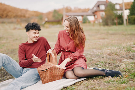 Young couple sharing a relaxed outdoor picnic, laughing and interacting naturally on a blanket, capturing emotional closeness and authenticity in a candid everyday moment.の写真素材