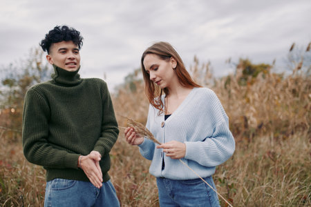 A young couple in a grassy field share a quiet, unposed moment that feels genuine and true to life, with natural expressions and relaxed body language reflecting authenticity and credibility.の写真素材