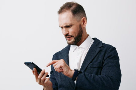 A focused businessman checks his phone, projecting confidence and concentration. He stands against an isolated colored background, creating a professional mood and clear, calm emotion.の写真素材