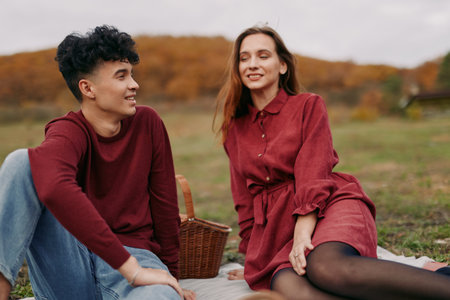 Young couple enjoying a candid autumn picnic on a blanket, sharing genuine smiles and relaxed conversation that convey authenticity and credibility in a natural lifestyle scene.の写真素材