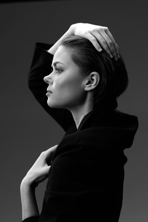 Black and white profile of a thoughtful woman in dark clothing with elegant pose and soft lightingの写真素材