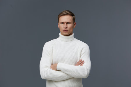 serious man in white turtleneck sweater stand arms crossed look camera confident dark gray background studio portrait concept mental health and gadgetsの写真素材