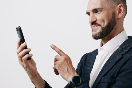 Professional man in business attire uses a smartphone, showing confident and thoughtful emotion, on an isolated colored background suitable for corporate or tech themes.の写真素材