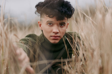 Close-up portrait of a young adult in tall dry grass, conveying a genuine unposed moment with...