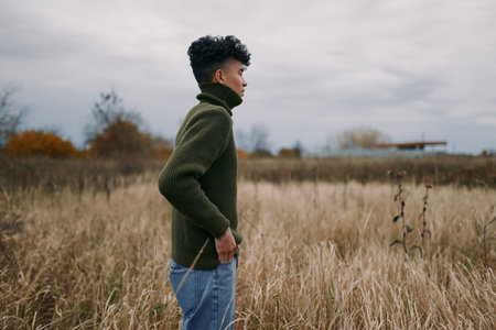 Side profile of a young man standing in tall autumn grass, candid pose and natural expression conveying authenticity and quiet confidence in a raw, credible outdoor portrait.の写真素材