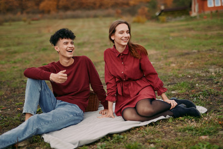 Two friends sit on a blanket outdoors, sharing a candid moment with genuine smiles and relaxed posture, capturing authenticity in everyday connection under soft light.の写真素材