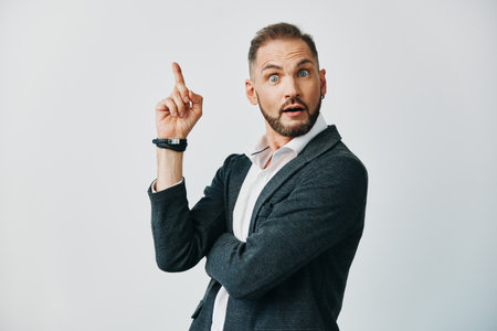An assertive business professional stands against a solid colored backdrop, capturing a surprised, alert moment as he points upward with one finger.の写真素材