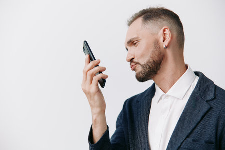 A professional man in a business suit examines a smartphone with focused emotion against a clean isolated colored background. The calm, confident pose conveys concentration, communication, andの写真素材