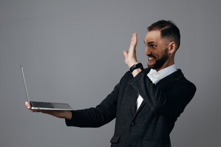 A professional business man on an isolated colored background, smiling as he waves with a laptop, conveying confidence, energy, and engaging communication.の写真素材