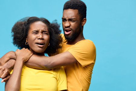 Two young African models express strong emotions in matching yellow shirts against a bright blue background, portraying a dramatic scene of tension and surpriseの写真素材