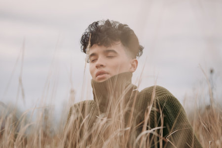 Portrait of a thoughtful youth in a windlit field, wearing a chunky knit turtleneck, eyes closed, conveying authenticity and credibility through natural pose and honest mood.の写真素材