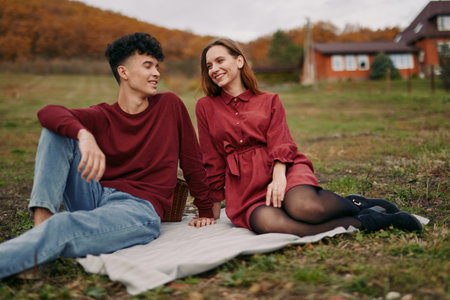Two friends sit on a blanket in a fall field, sharing a candid moment that emphasizes authentic connection and genuine ease, inviting trust and real emotion.の写真素材