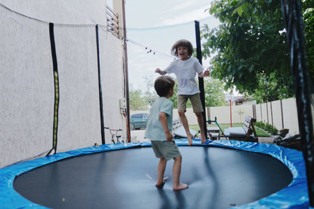 Happy children jumping on a trampoline, enjoying outdoor playtime in a sunny backyard, surrounded by greenery and laughter.の写真素材