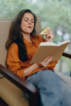 Young woman with long hair enjoying a book and sandwich in a cozy setting, exuding a relaxed and...