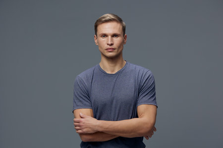 Confident young man with short hair wearing casual grey T-shirt looking directly at camera with...