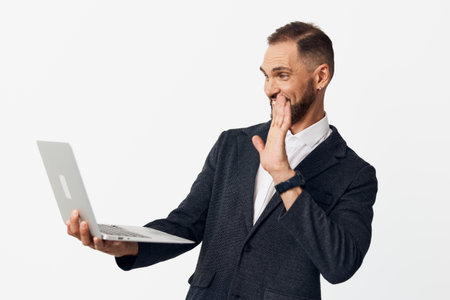 A professional man in a business suit uses a laptop, standing against a bright colored background, conveying focused attention, curiosity, and a friendly, confident smile in a moment of remote work.の写真素材