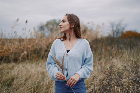 A candid portrait of a young woman standing in a windswept field, conveying natural gestures and subtle emotion with authenticity and reliable documentary style, soft autumn light.の写真素材