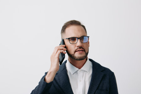 A professional man in business attire speaks on a cell phone against an isolated colored background,...