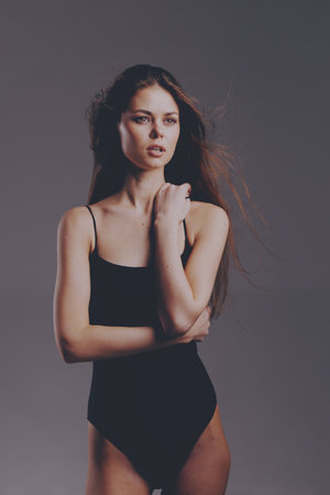 serious woman posing in black bodysuit with flowing hair against neutral background, fashion, beauty, eleganceの写真素材