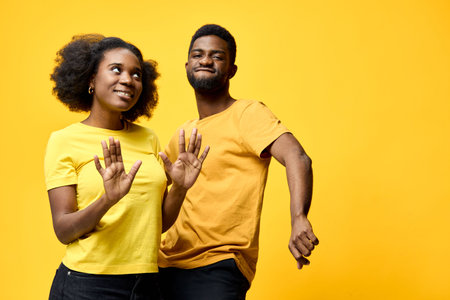 Happy African couple dancing joyfully in matching yellow outfits against a bright yellow background, showcasing vibrant emotions and dynamic movementの写真素材