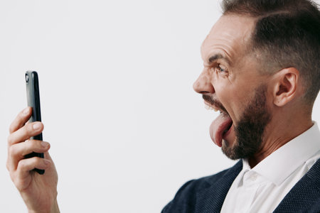 A professional business man on an isolated colored background, expressing confidence and curiosity as he engages with a smartphone for a candid self recording.の写真素材