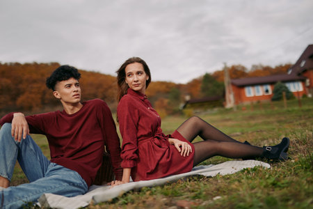 Young couple lounging on a picnic blanket in a countryside field, photographed with authenticity and credibility in a candid, natural composition that highlights relaxed connection and genuineの写真素材