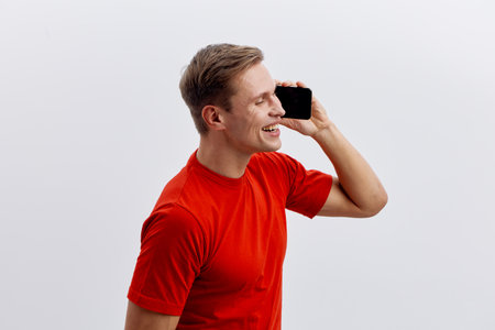 smiling young caucasian man wear red shirt hold smartphone speak phone digital nomad remote work conceptの写真素材