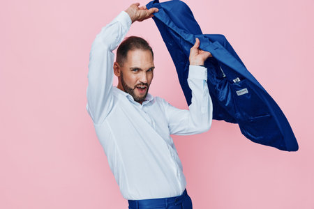 A confident male professional shows energy in a vibrant pink studio, lifting a blue jacket overhead. The isolated colored background highlights motion, ambition, and focus.の写真素材