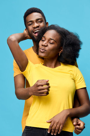 Joyful couple embracing against a blue background, wearing bright yellow and orange shirts, depicting love and happiness in a vibrant and cheerful atmosphereの写真素材