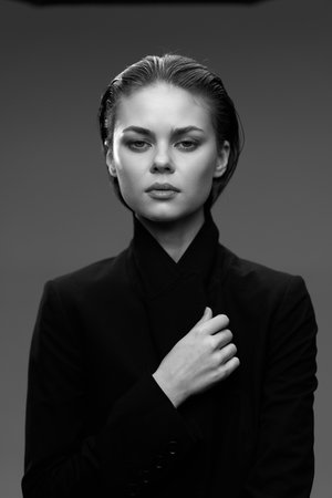 Black and white portrait of a serious woman with slicked-back hair wearing a black suit on a plain backgroundの写真素材