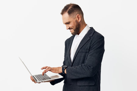 A professional business man stands with a laptop on a isolated colored background, showing focus, confidence and curiosity while engaging with technology.の写真素材