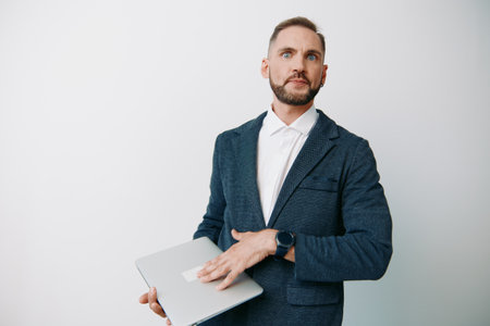 A professional businessman stands against an isolated colored background, holding a laptop with calm confidence. His poised posture suggests readiness for strategy, meetings, and leadership tasks.の写真素材