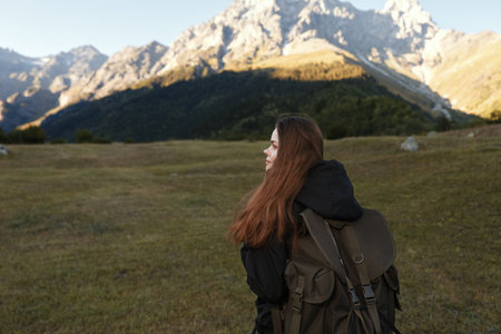 A lone traveler with a backpack stands in a grassy field, looking toward distant mountains under a...