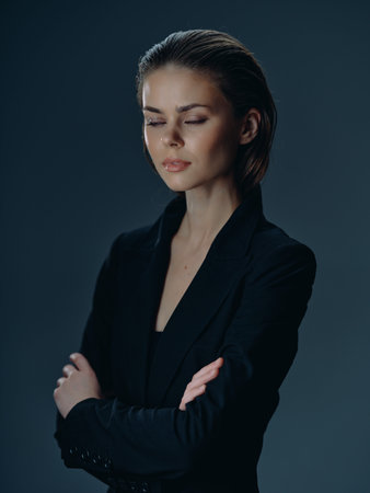 Young woman in black suit with crossed arms and closed eyes showing calm and confidence in dark studio settingの写真素材